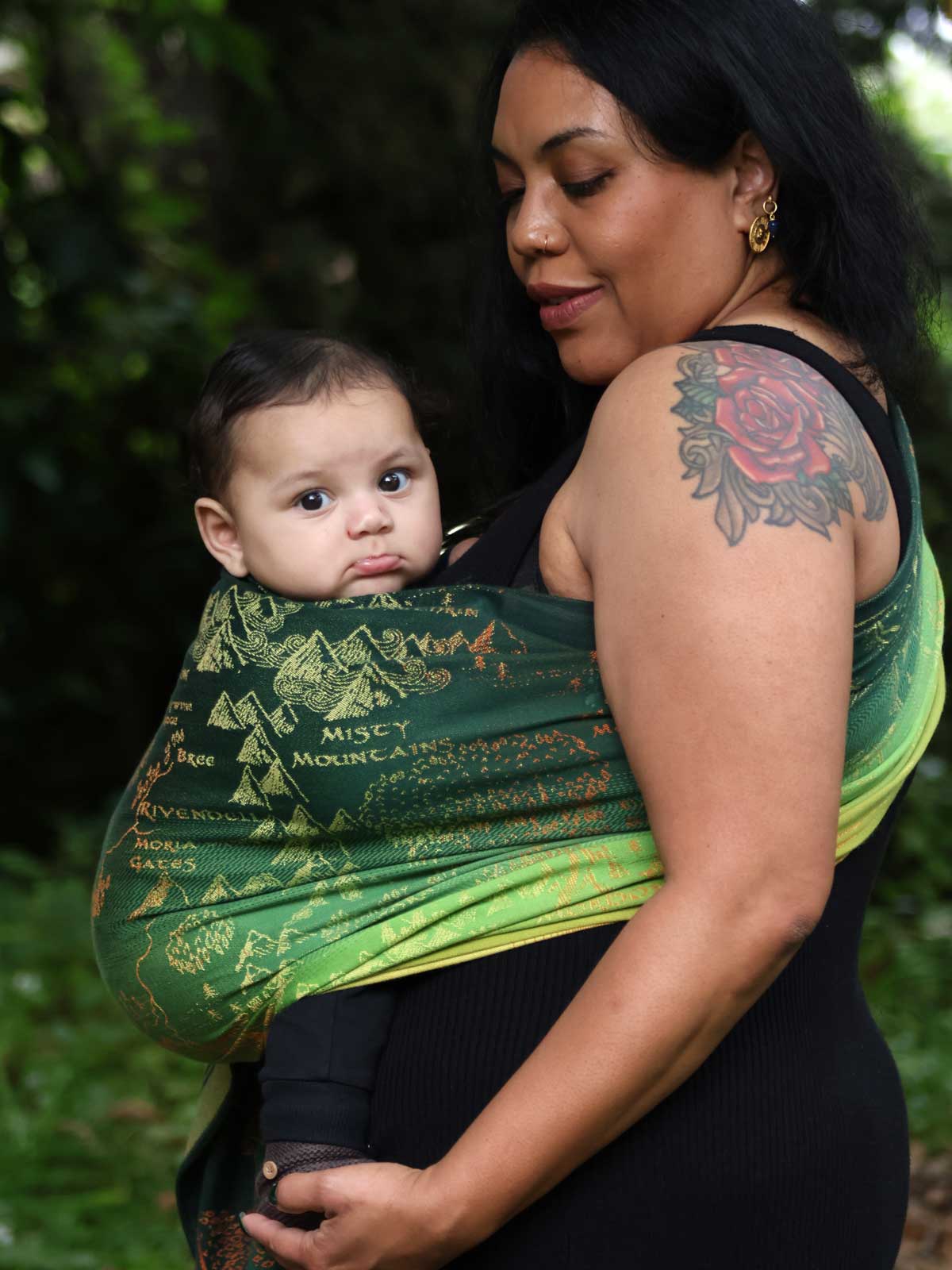 Woman carrying a baby in a green ring sling with map design.