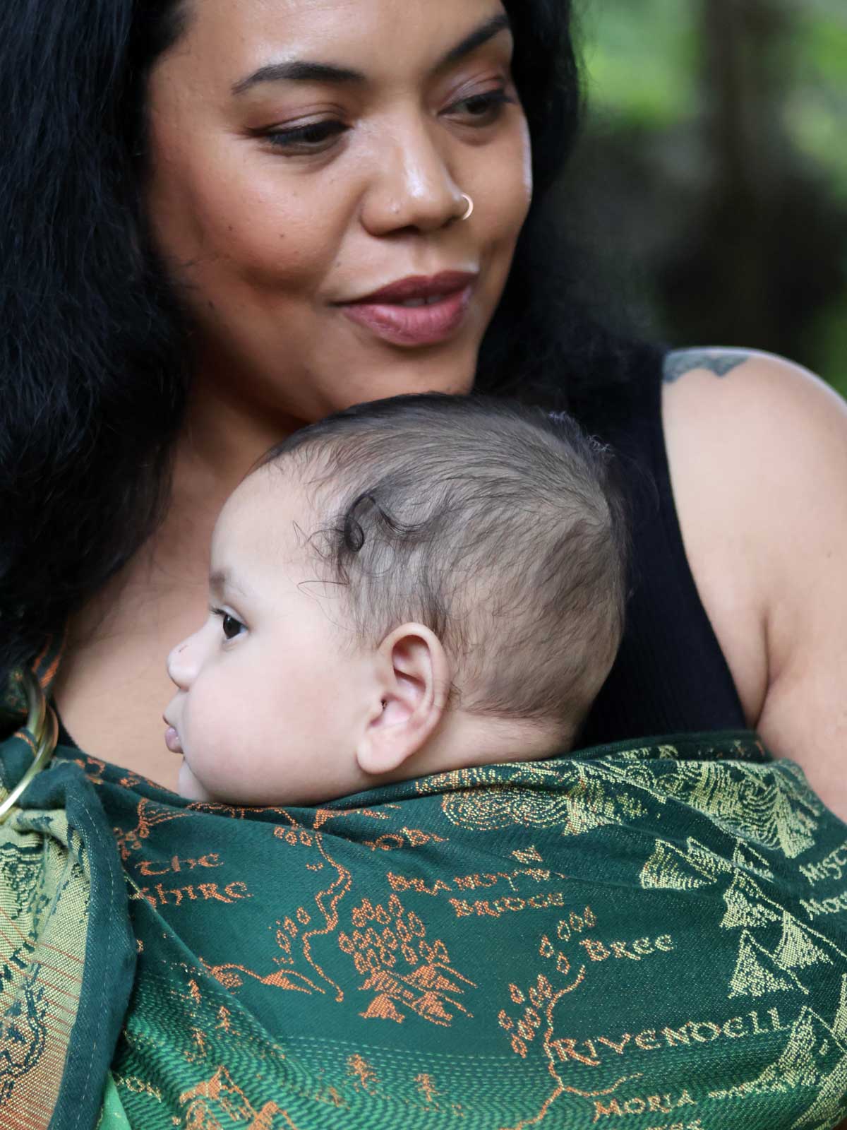 Close up of a woman carrying a baby in a green ring sling with map design.