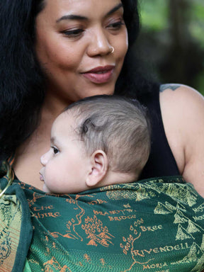 Close up of a woman carrying a baby in a green ring sling with map design.