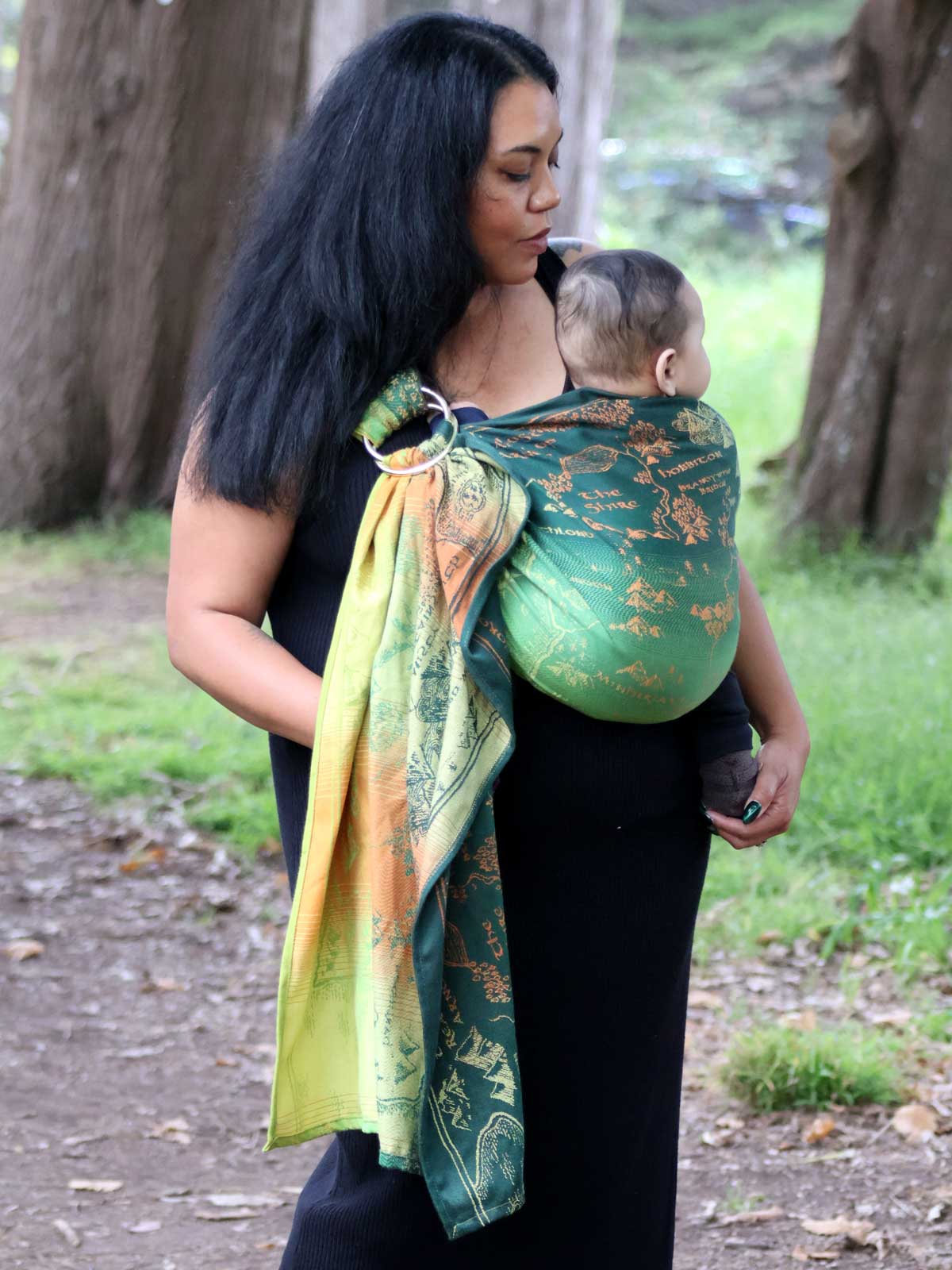 Woman carrying a baby in a green ring sling with map design.