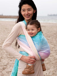 Woman carrying a child on a beach using a colourful baby carrier.