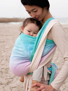 Woman holding a baby in a sling on a beach