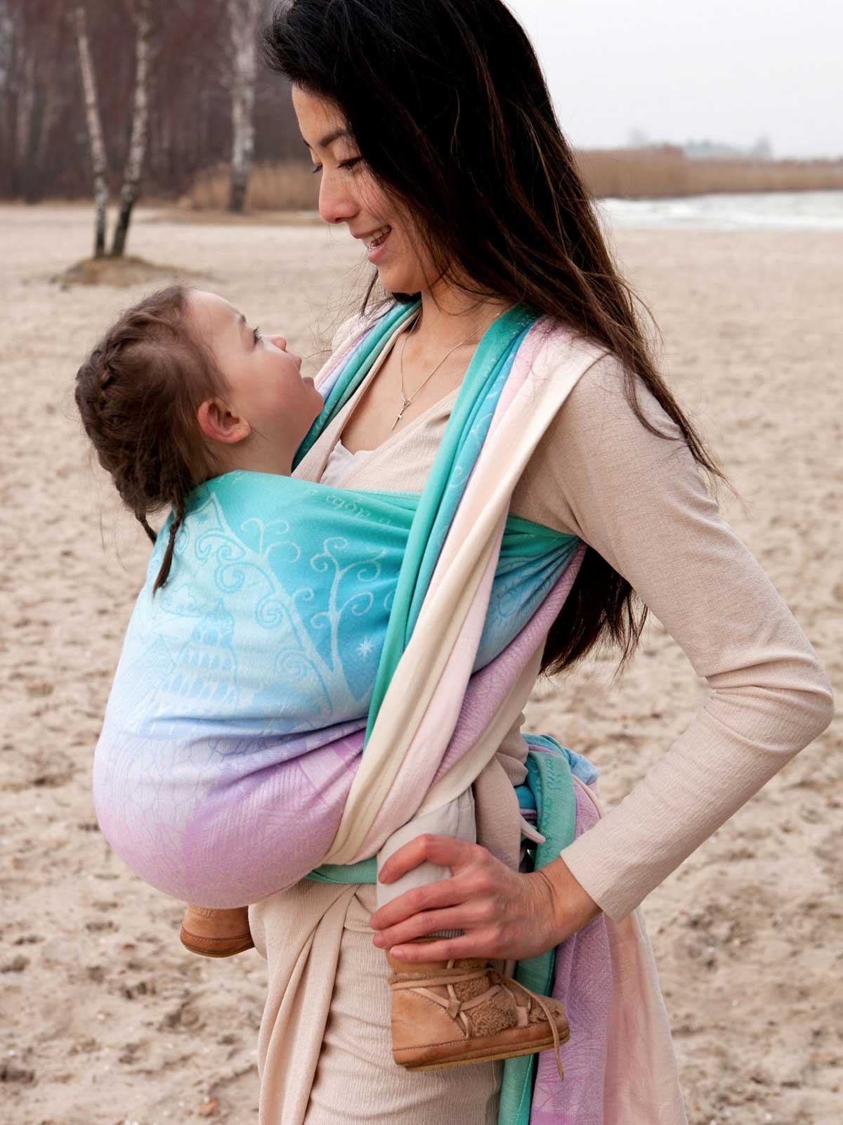 Woman carrying a baby in a sling on a sandy beach