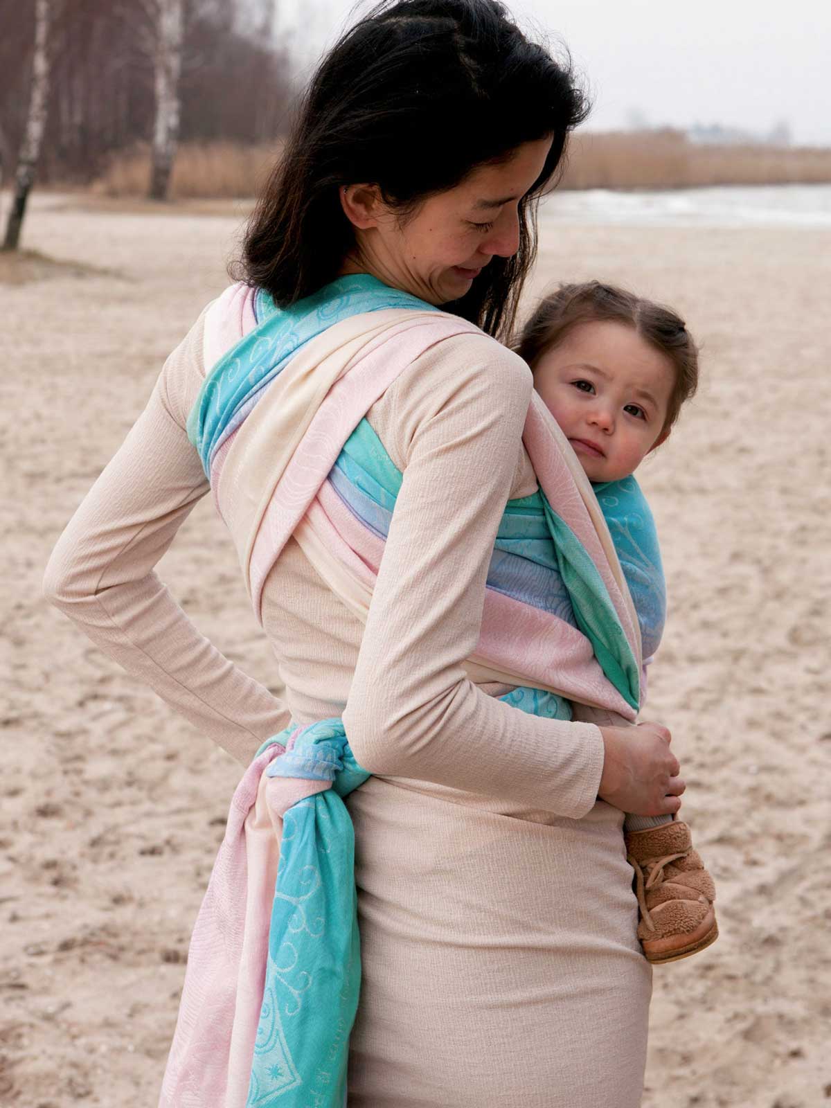 Woman carrying a child on a beach using a colorful wrap
