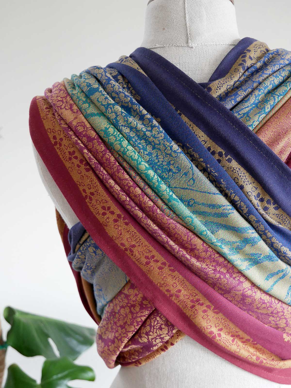 Mannequin wearing a colorful baby wrap with various patterns on a white background