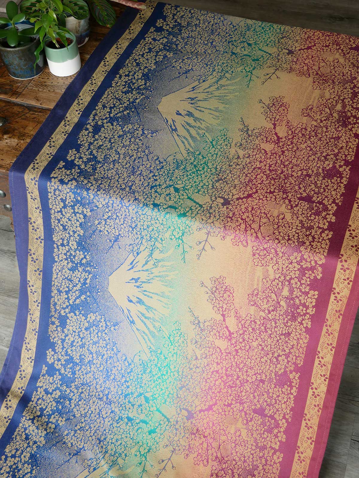 Colourful floral-patterned fabric on a wooden table with plants in the background