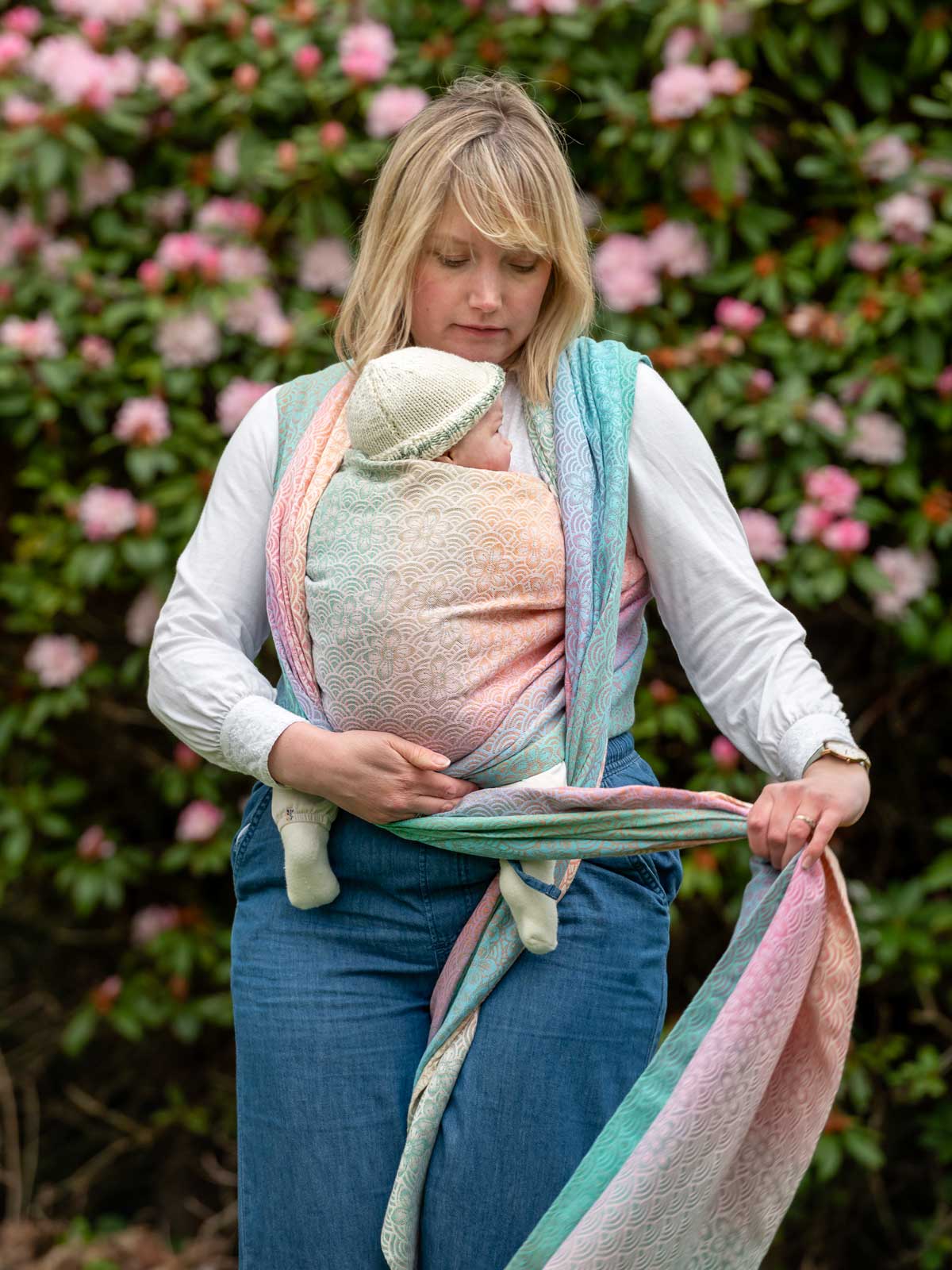 Woman holding a baby wrapped in a colorful sling against a floral background