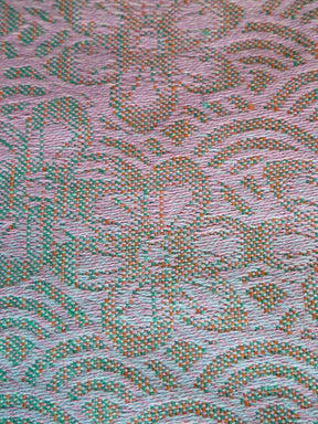 Textured fabric with a pattern of green and orange lines on a pink background