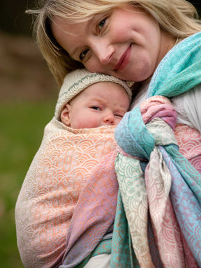 Woman holding a baby wrapped in a colorful woven wrap outdoors