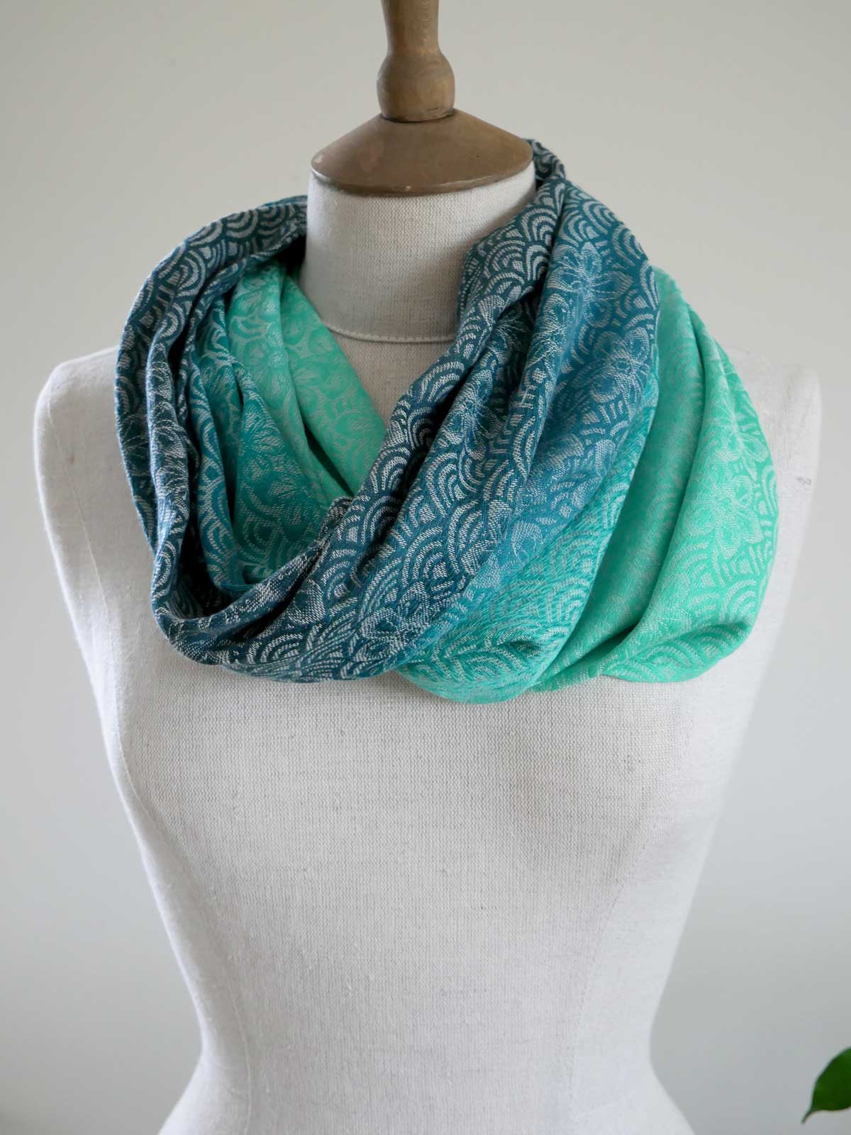 Turquoise and teal patterned Sekaibloom Wave Cowl on a mannequin against a white background