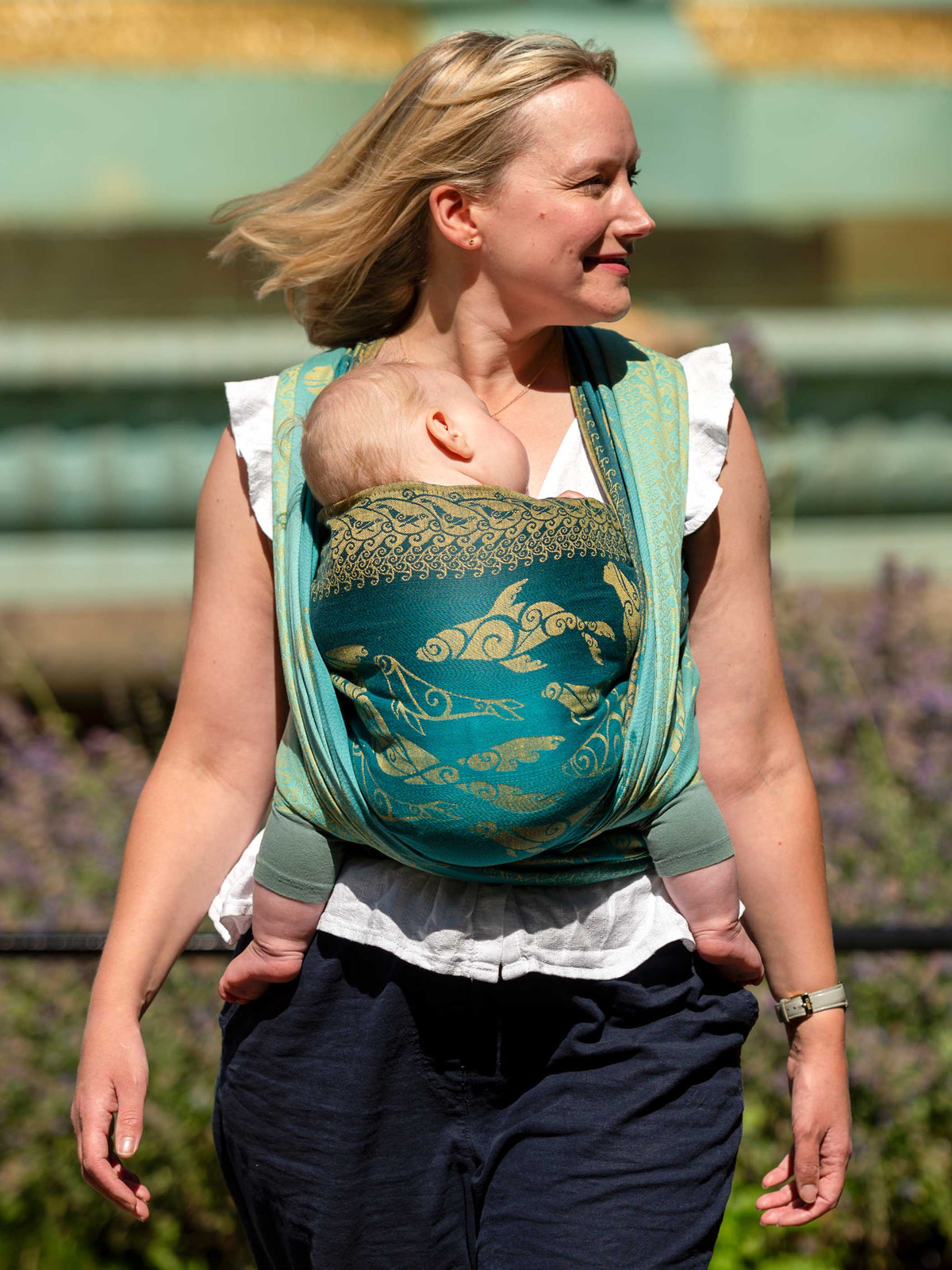 A woven carrying a baby in a teal woven wrap with gold Selkies