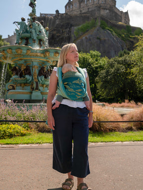 Woman carrying a baby in a teal wrap with Edinburgh Castle in the background