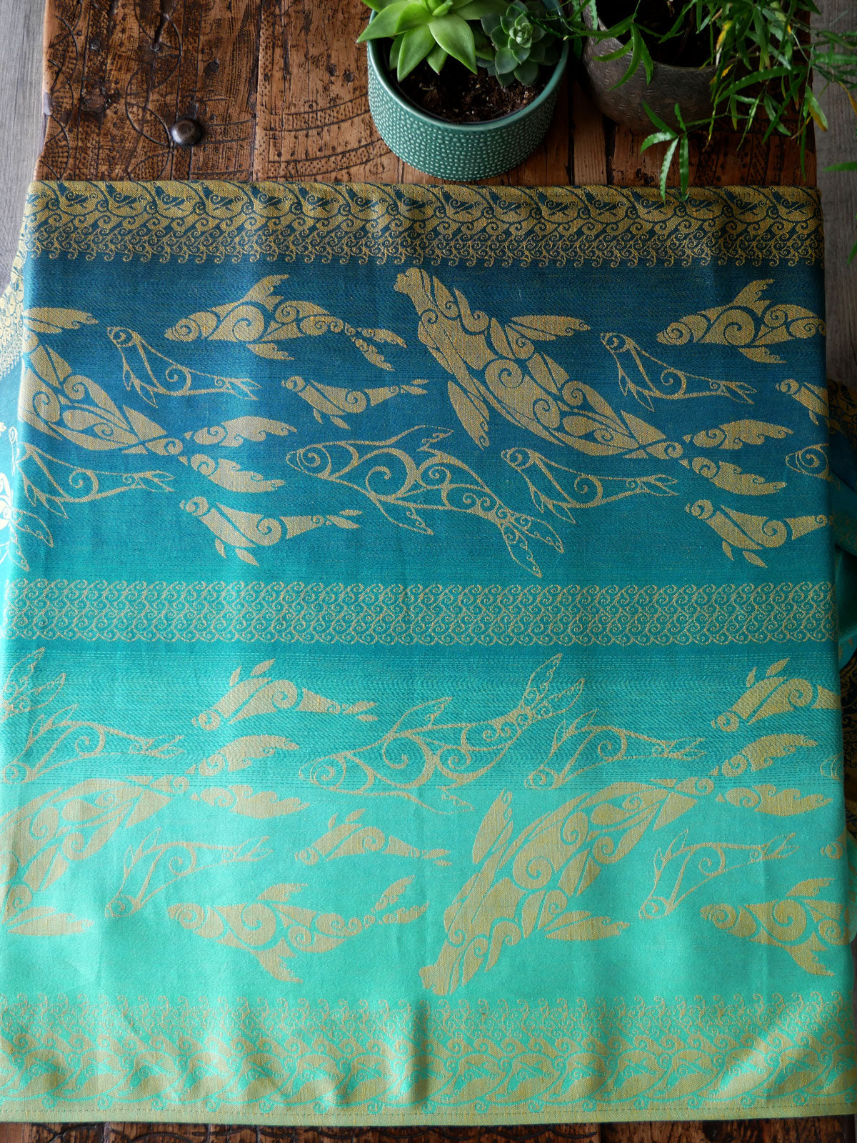 Turquoise fabric with gold seal pattern on a wooden surface with plants.