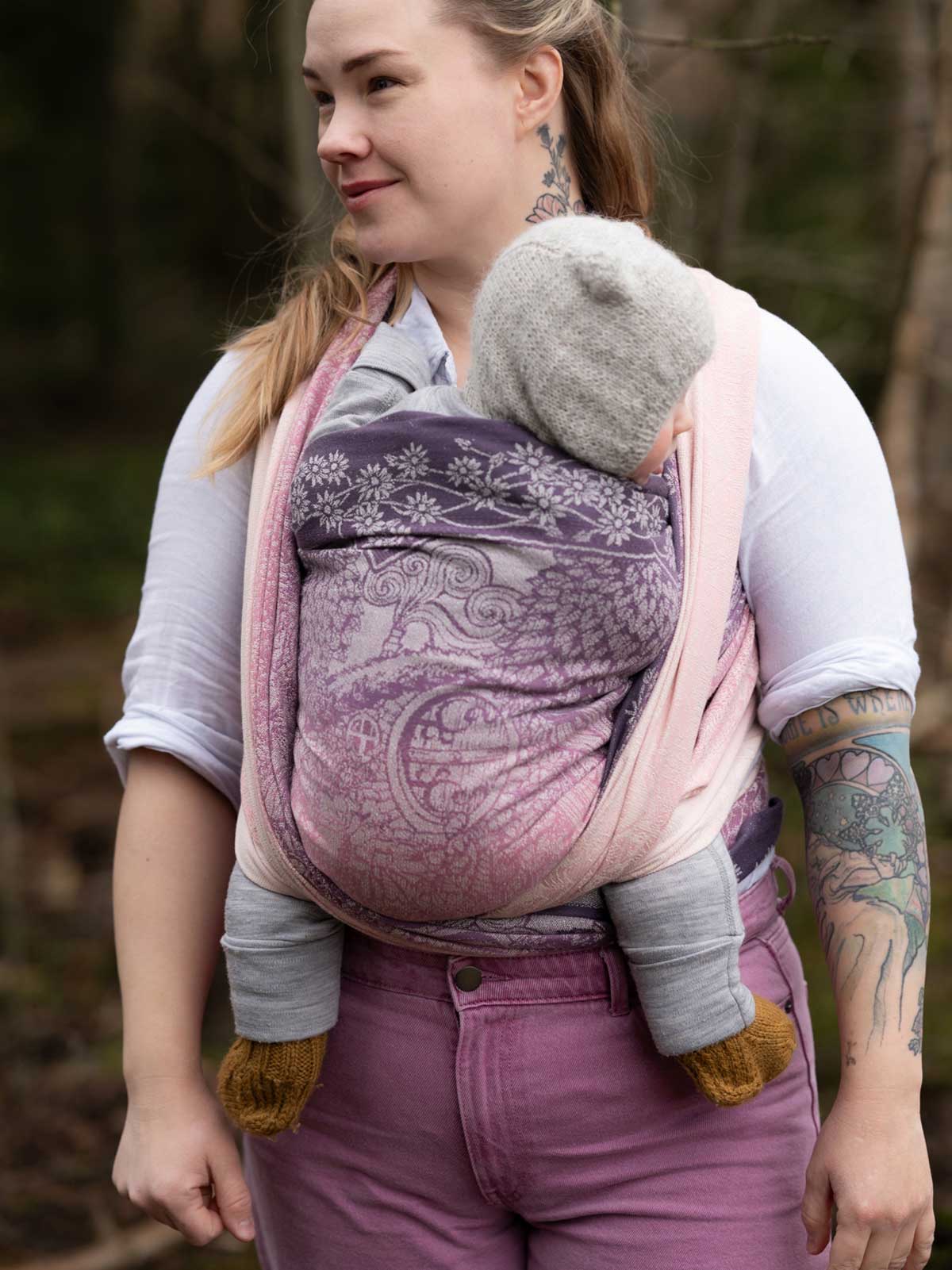 Woman carrying a baby in a purple baby carrier outdoors.