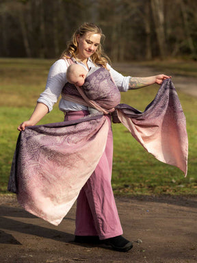 Woman holding a large, patterned baby wrap outdoors with a natural background