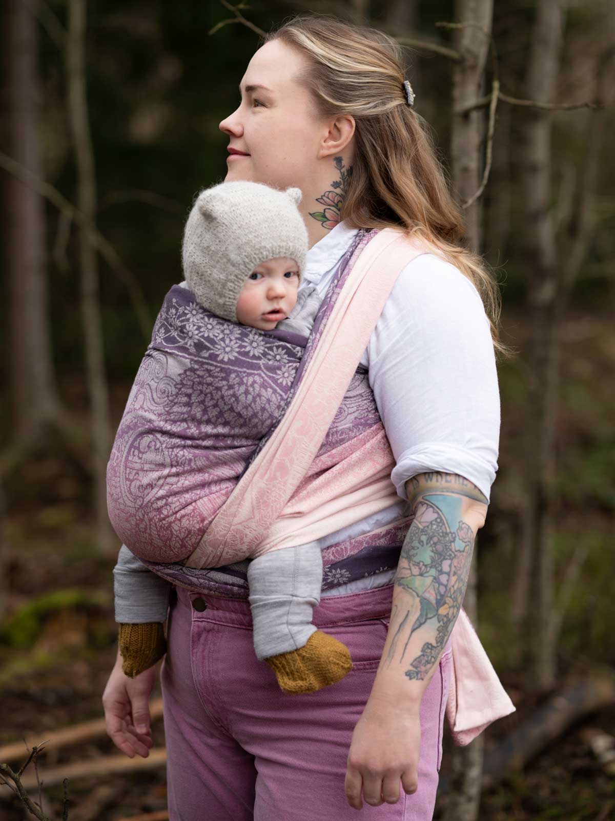 Woman carrying a baby in a sling outdoors in a forest setting