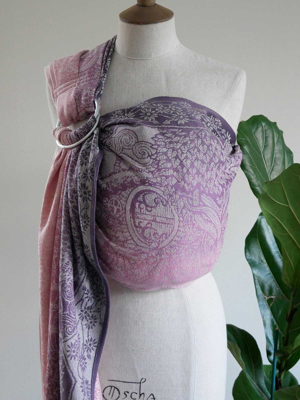 Mannequin wearing a purple and pink patterned ring sling with a plant in the background