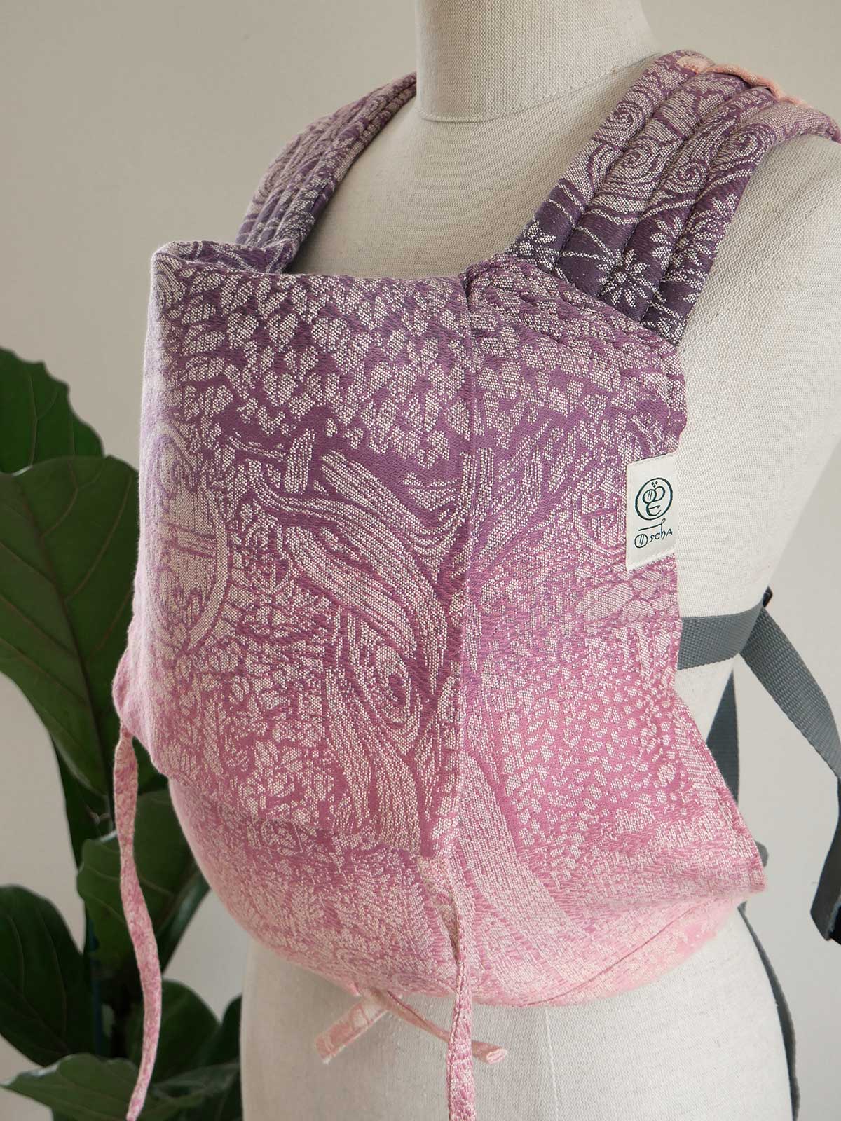 Pink patterned baby carrier on a mannequin with a plant in the background