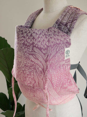 Pink patterned baby carrier on a mannequin with a plant in the background