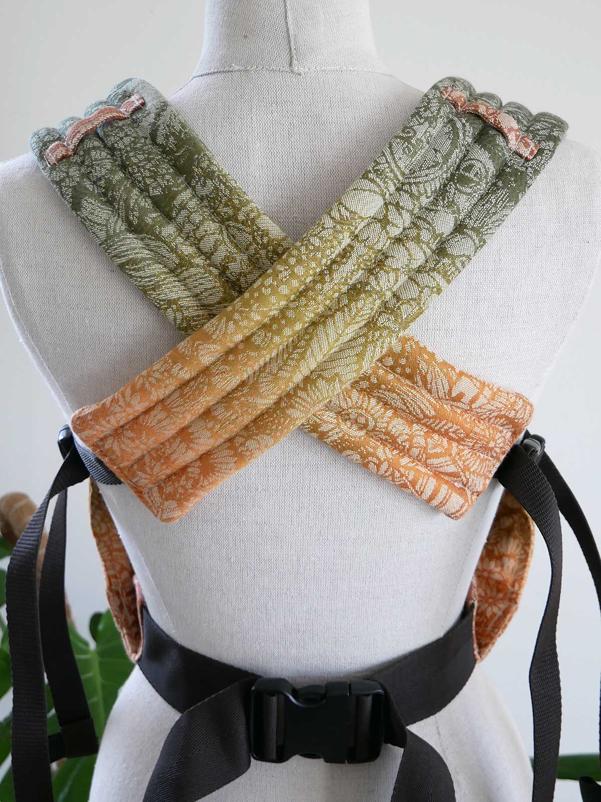 Mannequin wearing a baby carrier with green, yellow, and orange patterns on a white background.