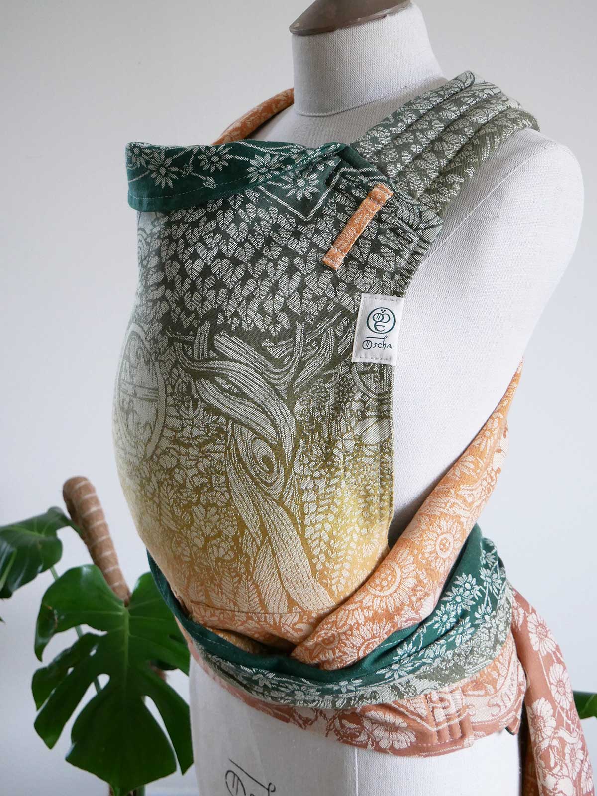 Mannequin wearing a patterned baby carrier with a plant in the background
