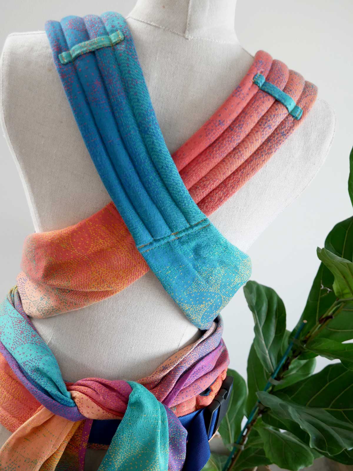 Colorful baby carrier on a mannequin with a plant in the background