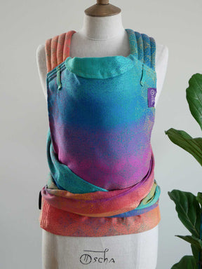 Colorful baby carrier on a mannequin with 'Oscha' branding against a neutral background.