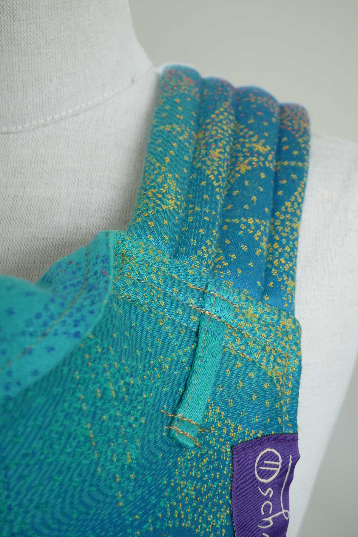 Close-up of a teal and yellow patterned garment with a visible brand logo on a white background