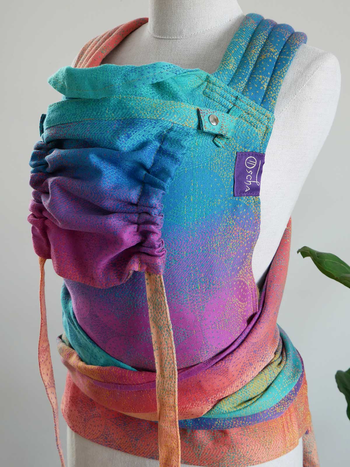 Colorful baby carrier on a mannequin with a visible brand label against a neutral background
