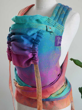Colorful baby carrier on a mannequin with a visible brand label against a neutral background