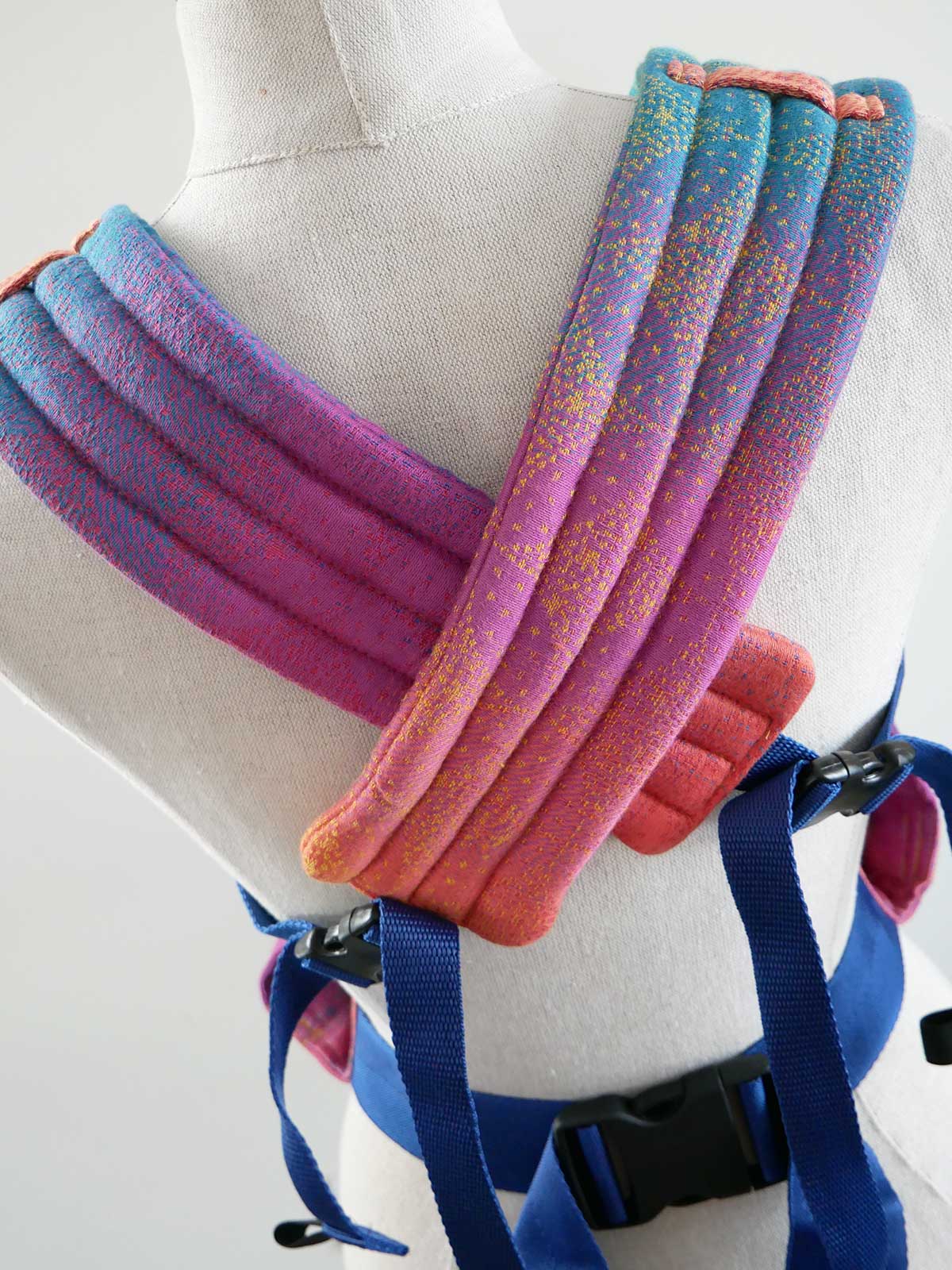 Colorful baby carrier wrap on a mannequin with blue straps.