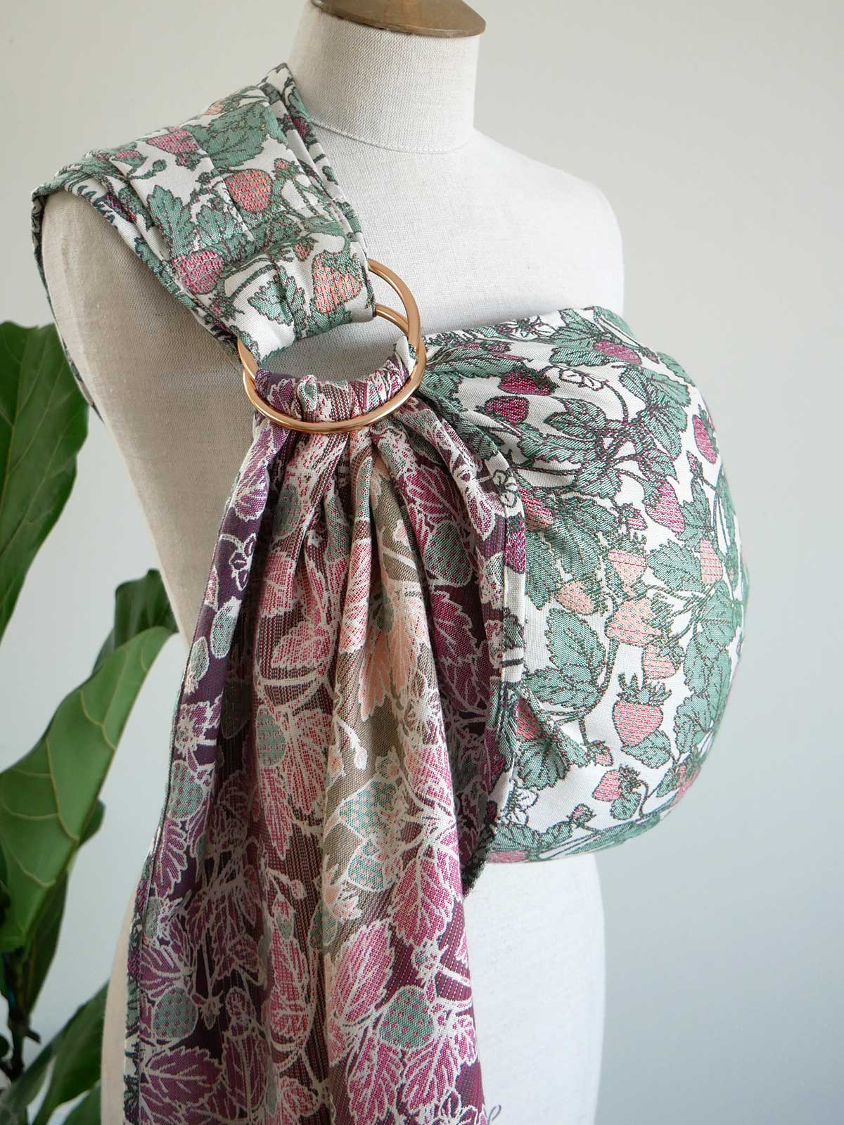 Mannequin wearing a strawberry-patterned ring sling with a green plant in the background
