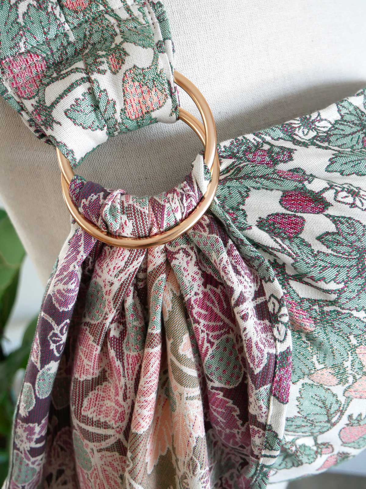 Strawberry-patterned ring sling with a gold ring tied through it on a neutral background