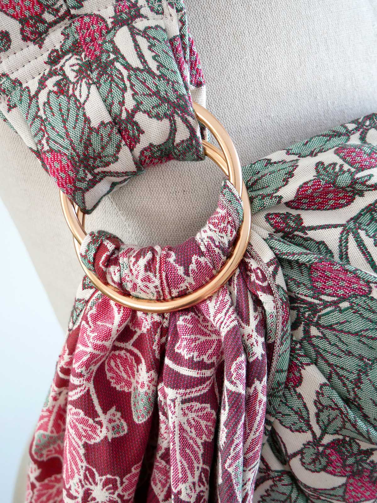 Close-up of a strawberry patterned ring sling with a gold ring detail on a neutral background