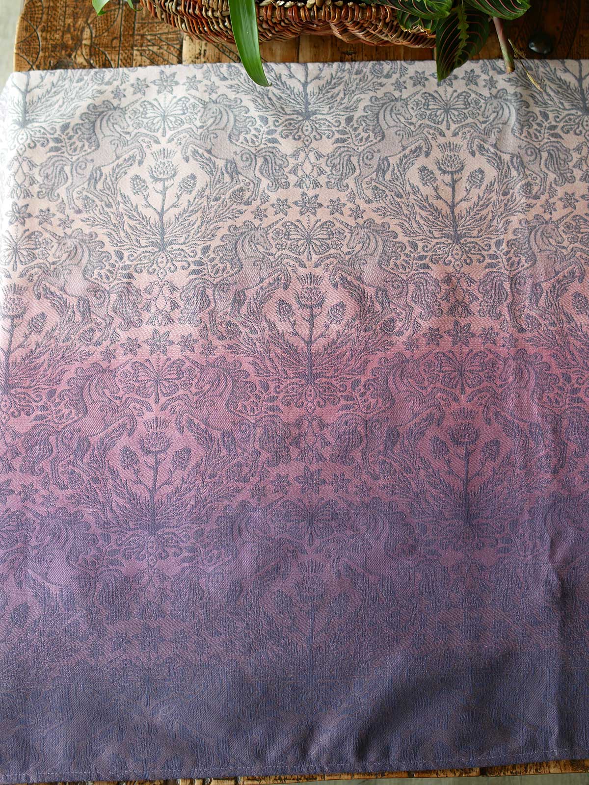 Woven fabric in pinks and purples with a unicorn pattern laid flat on a wooden table