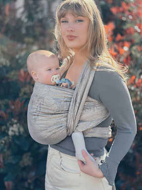Woman holding a baby in a sling against a blurred natural background