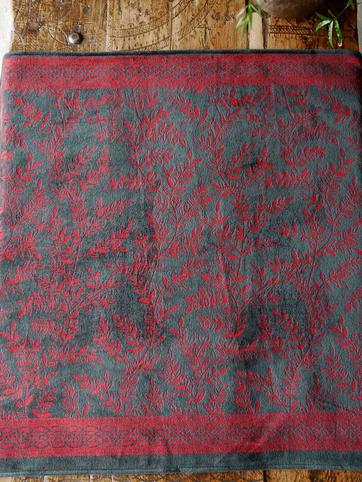 Textile with red floral pattern on a gray background, displayed on a wooden surface.