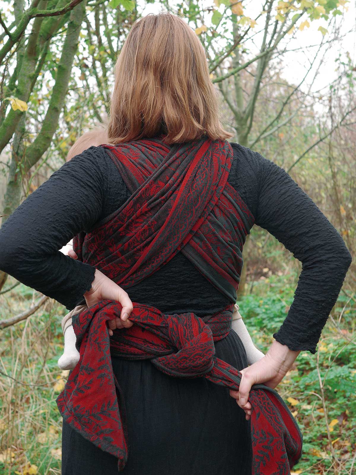 Person wearing a red and black patterned wrap in a forest setting