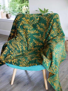 Green throw with golden willow leaves design. The throw is draped over a chair.
