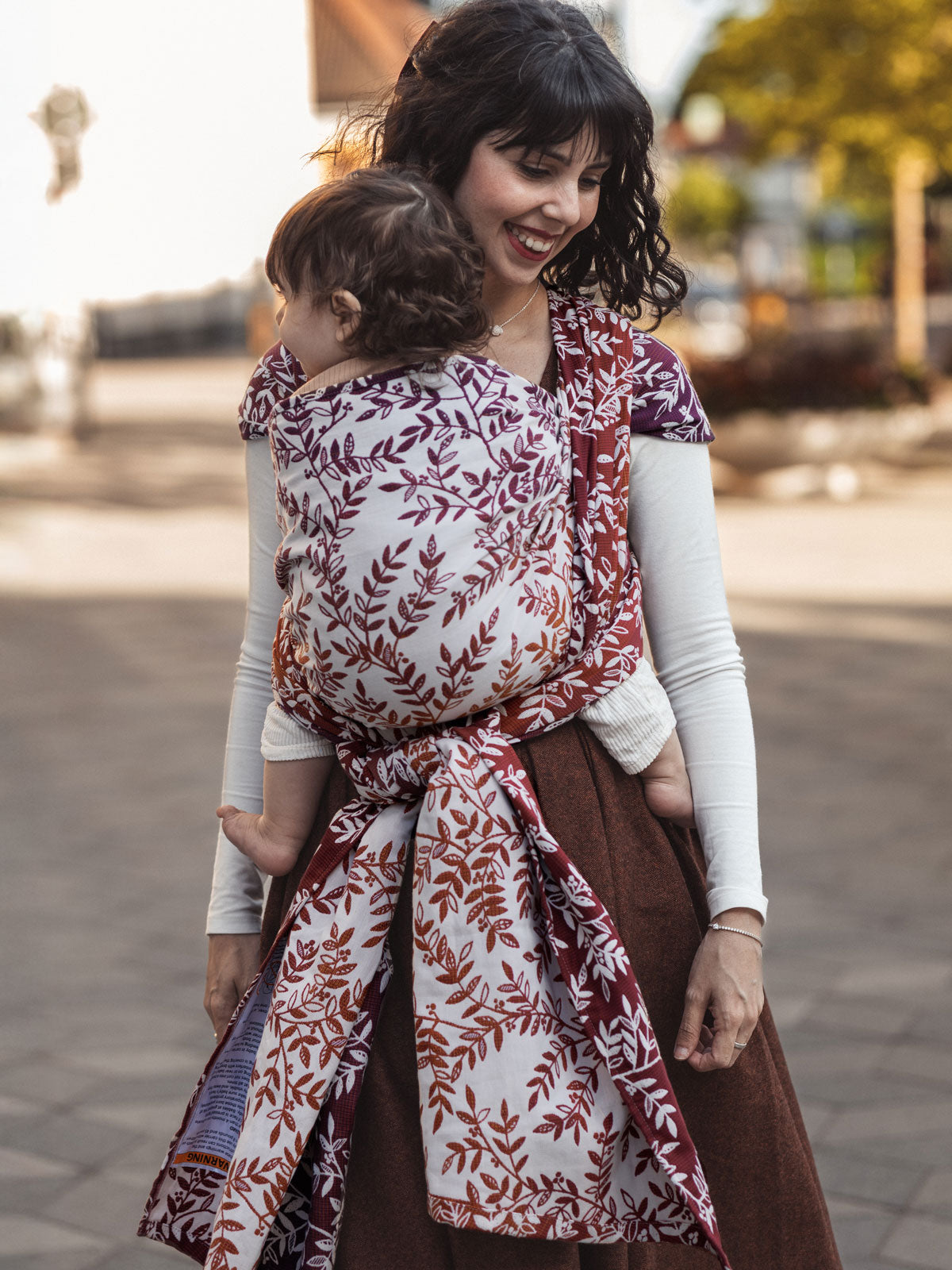 Woman carrying a child in a floral baby woven wrap outdoors.