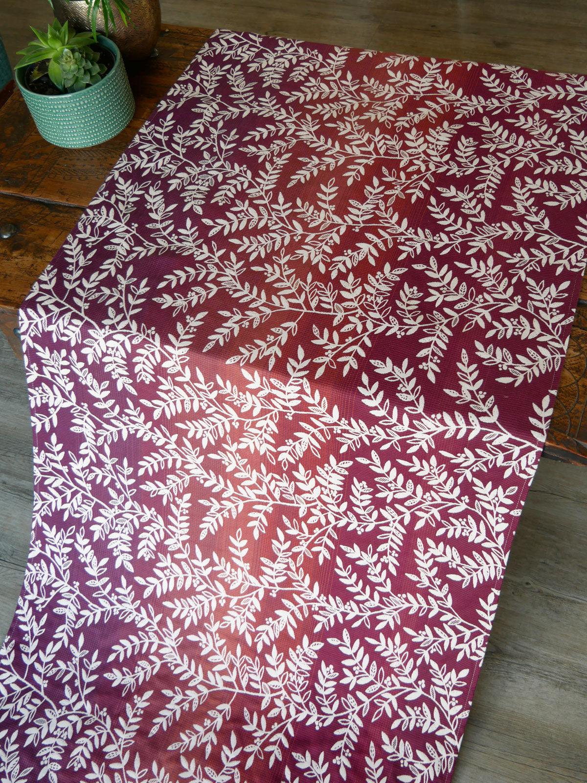 Burgundy purple fabric with white leaf pattern on a wooden surface