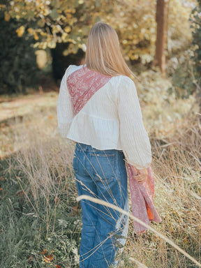 Person wearing a white blouse and blue jeans standing in a natural setting.