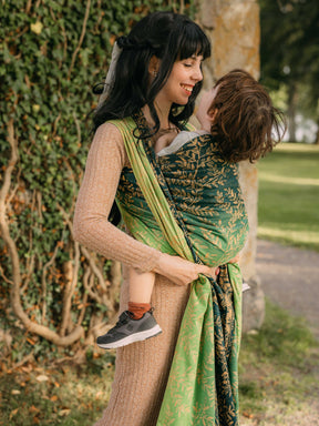 Side view of a woman carrying a child in a green woven wrap with gold leaf pattern