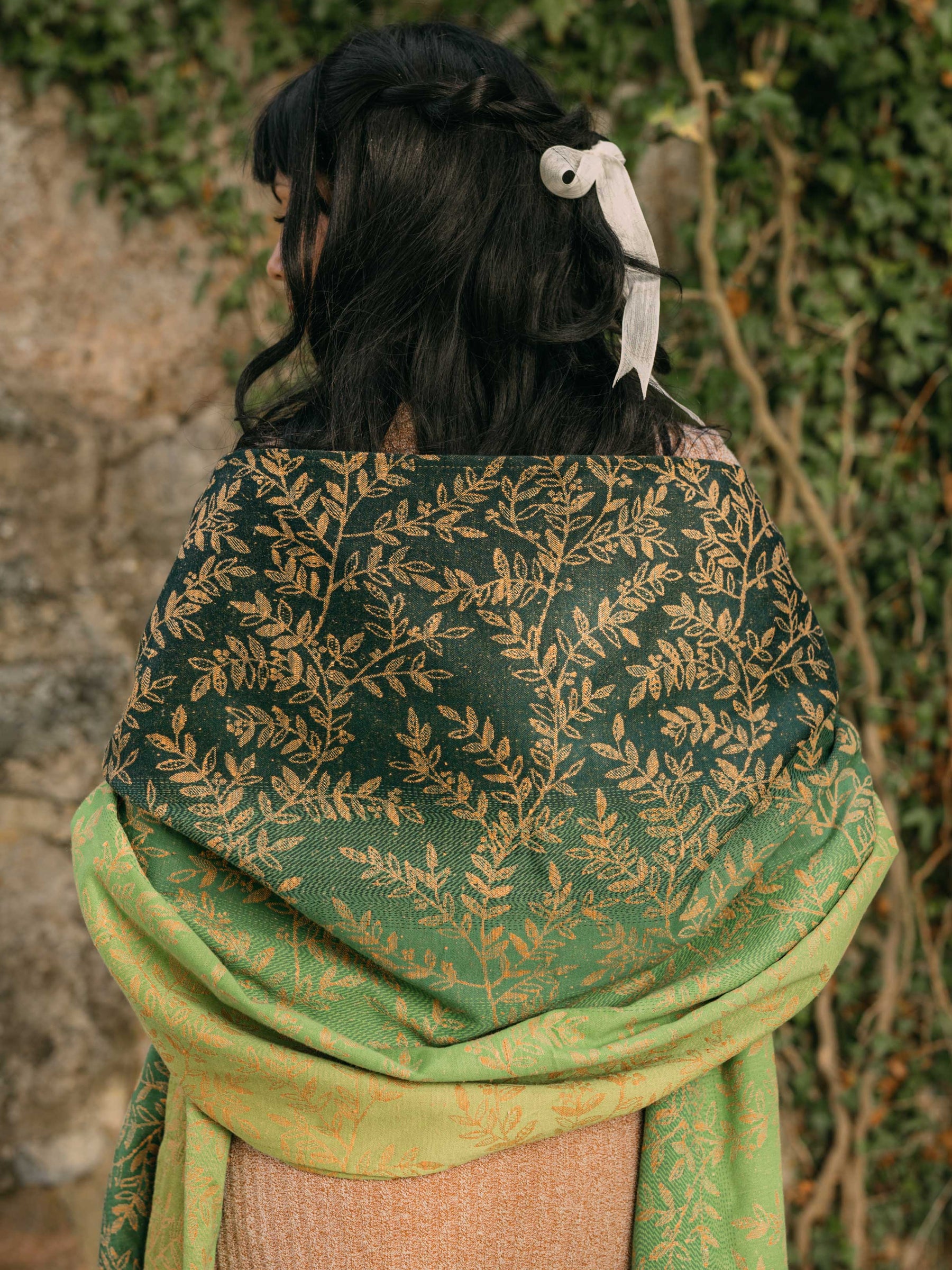 The back of a woman wearing a green shawl with gold leaf pattern 