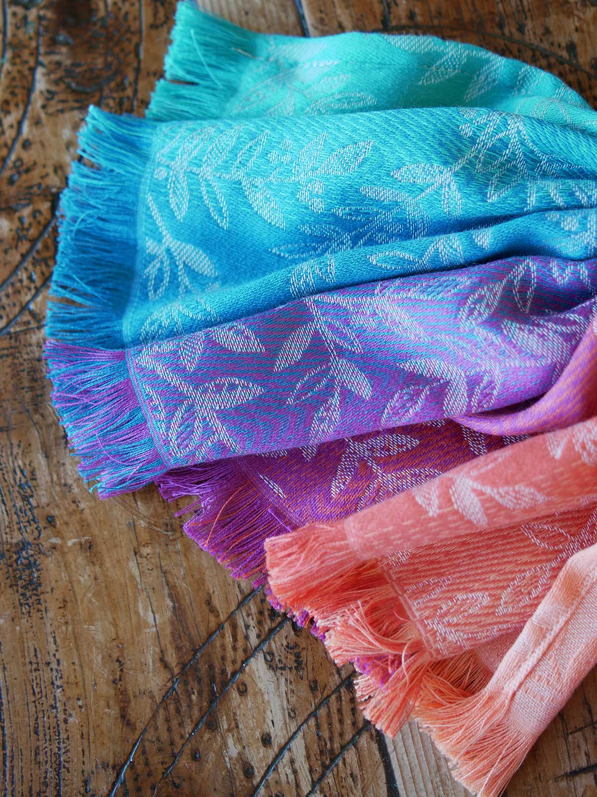 Stack of colorful scarves with floral patterns on a wooden surface