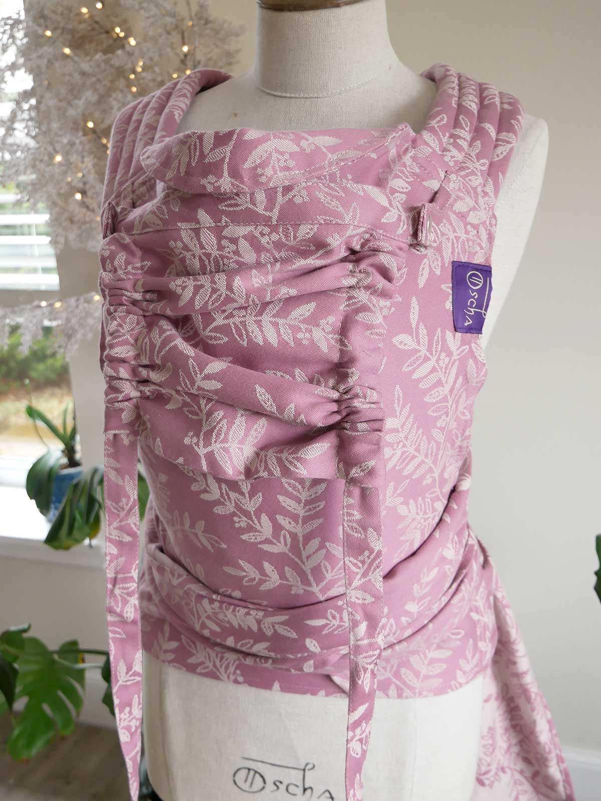 Pink floral baby carrier on a mannequin with a blurred indoor background