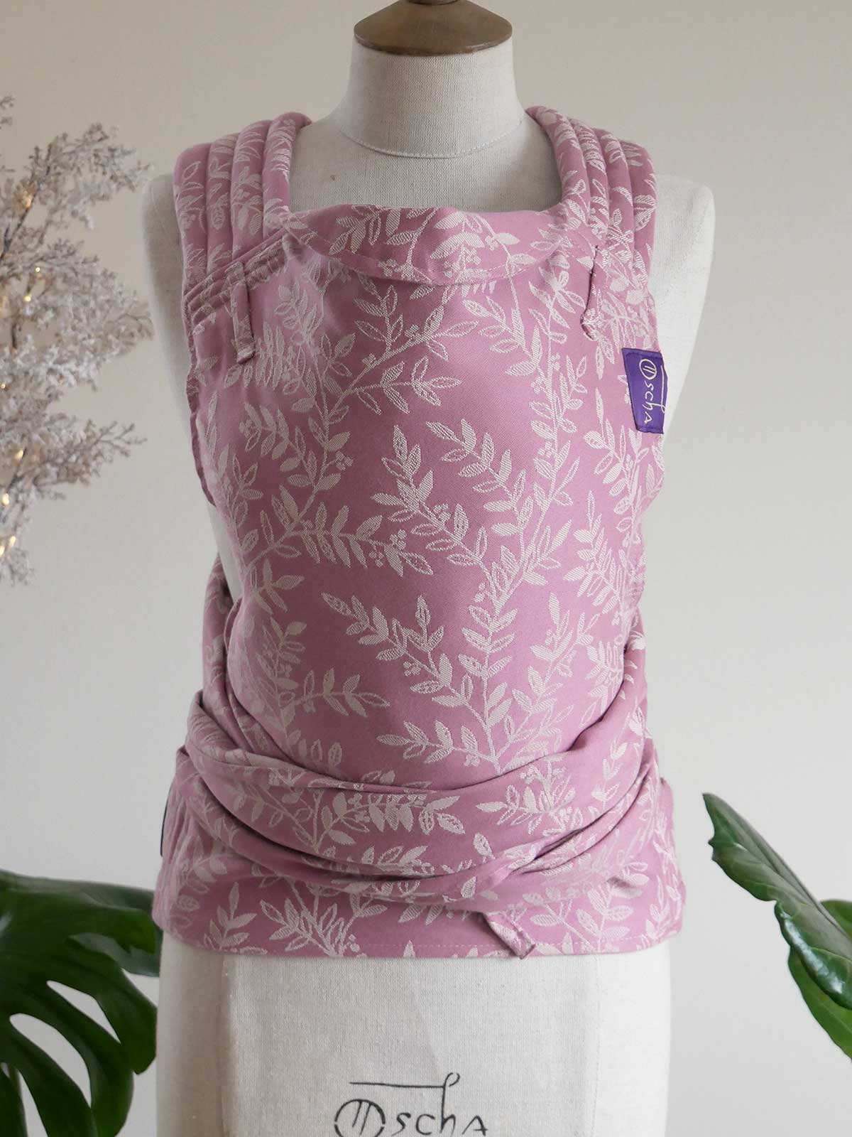Pink baby carrier with white leaf pattern on a mannequin against a white background