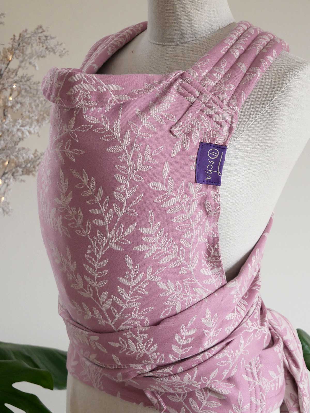 Pink baby carrier with leaf pattern on a mannequin against a neutral background