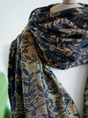 Close up of a black scarf with golden leaves draped on a mannequin