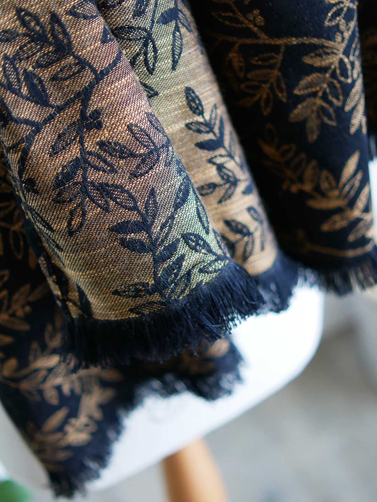 Close up of fringing on a black scarf with golden leaves draped on a mannequin